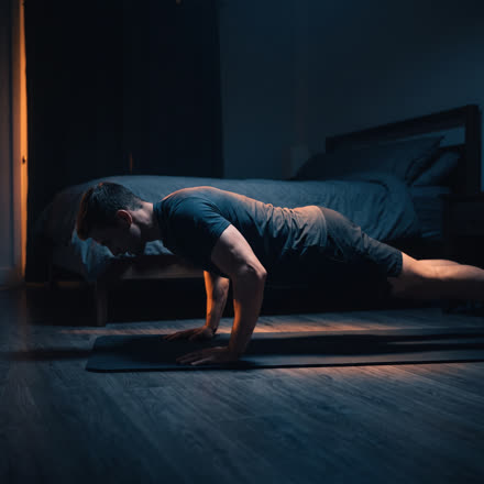 A man doing a push-up on a mat in a dark bedroom